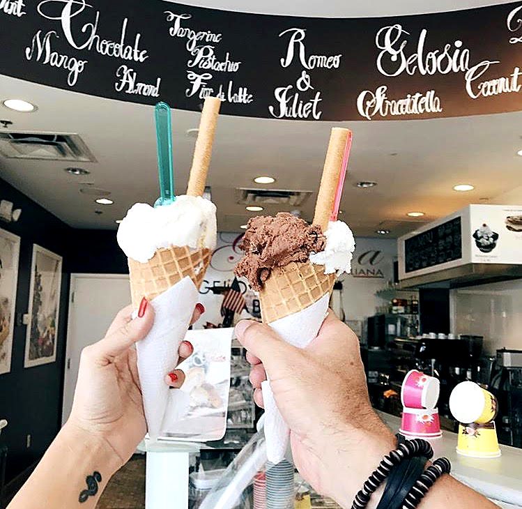Two gelato cones raised in front of the Gelosia flavor board